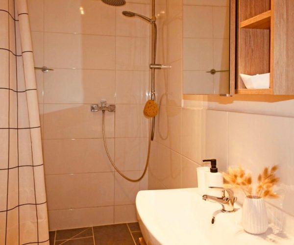 Modernes, kleines Badezimmer in einer Ferienwohnung mit einer Dusche, die durch einen Duschvorhang mit Gittermuster abgetrennt ist.