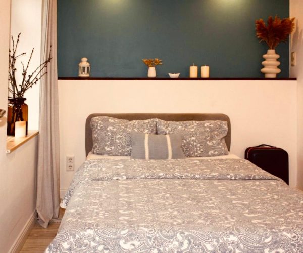 Schlafzimmer in einer Ferienwohnung mit einem großen Bett, bezogen mit einer grau-gemusterten Decke und Kissen.