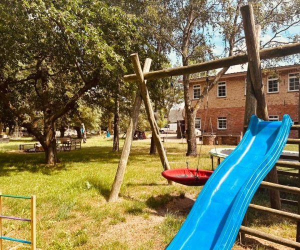Großer, weitläufiger Garten einer Ferienunterkunft mit einem Spielplatz, der eine blaue Rutsche und eine rote Schaukel umfasst.