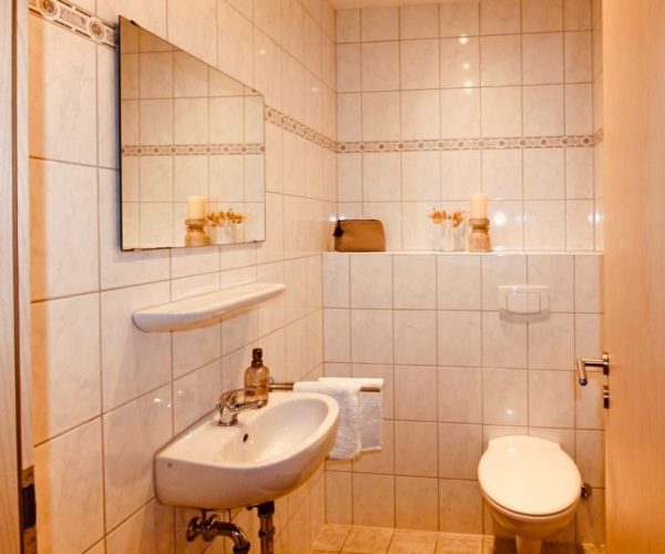 Kleines, helles Badezimmer in einer Ferienwohnung mit beigefarbenen Fliesen und einer dekorativen Bordüre.