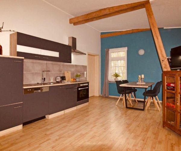 Offene Küche und Essbereich in einer Ferienwohnung mit modernem, dunkelgrauem Küchenblock und hellen Holzböden.