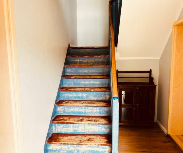 Rustikale Holztreppe in einer Ferienwohnung mit abgenutzter blauer Farbe auf den Stufen und sichtbarem Holz.