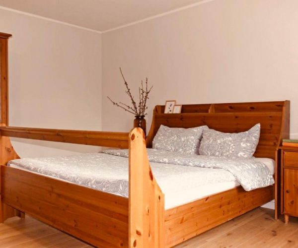 Schlafzimmer in einer Ferienwohnung mit einem großen, rustikalen Doppelbett und einem Kleiderschrank aus hellem Holz mit integriertem Spiegel.