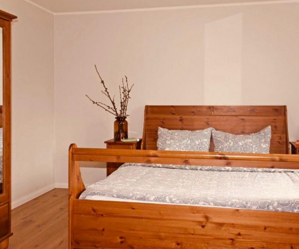 Schlafzimmer in einer Ferienwohnung mit einem großen, rustikalen Doppelbett und einem Kleiderschrank aus hellem Holz mit integriertem Spiegel.
