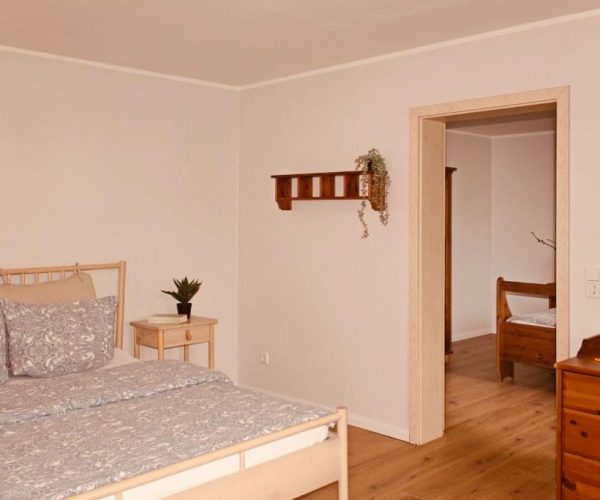 Helles und freundliches Schlafzimmer in einer Ferienwohnung mit einem Doppelbett in hellem Holz und grauer, gemusterter Bettwäsche.