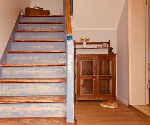 Rustikale Holztreppe in einer Ferienwohnung mit abgenutzter blauer Farbe auf den Stufen und sichtbarem Holz.