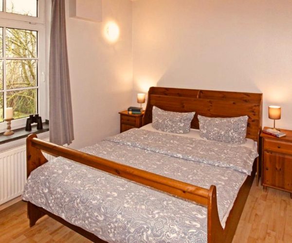 Schlafzimmer in einer Ferienwohnung mit einem rustikalen Doppelbett aus Holz, bezogen mit grauer, gemusterter Bettwäsche.