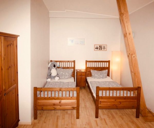 Schlafzimmer in einer Ferienwohnung in Sellin mit zwei rustikalen Einzelbetten aus Holz, bezogen mit grauer, gemusterter Bettwäsche.