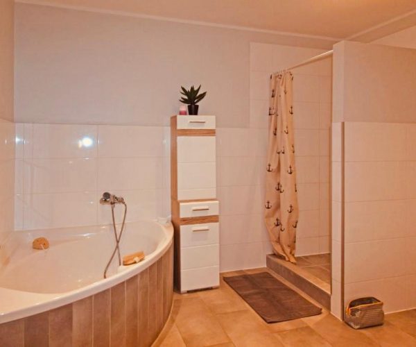 Badezimmer in einer Ferienwohnung mit einer großen Eckbadewanne und einer Duschkabine mit einem Duschvorhang mit Anker-Motiv.